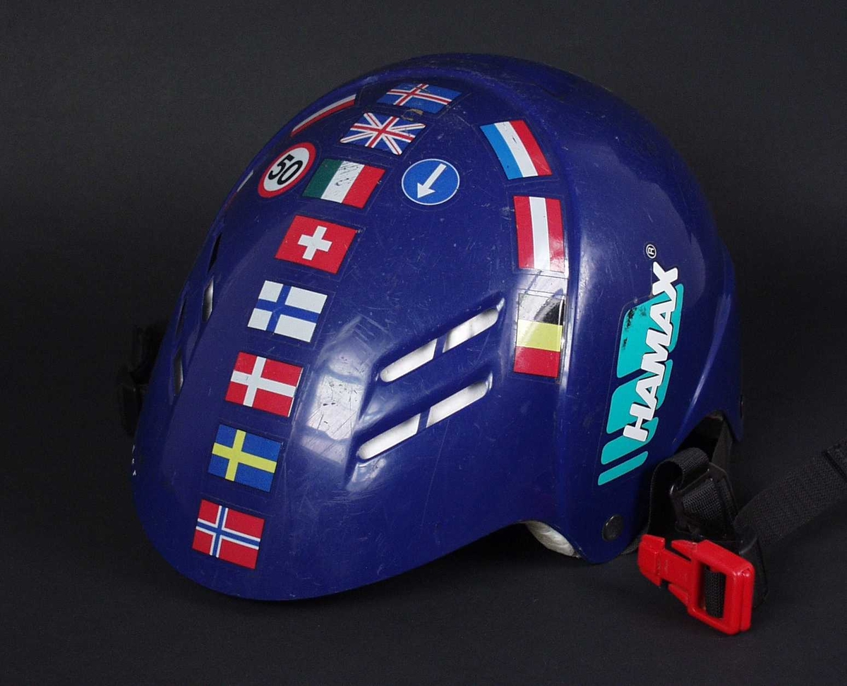 Blå sykkelhjelm av plast og isopor med rem under haka. Hjelmen har klistremerker med flagg og trafikkskilt.