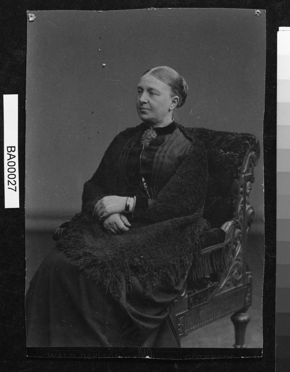 Portrett av eldre dame i sort med sort sjal sittende i stor lenestol i kvartprofil.