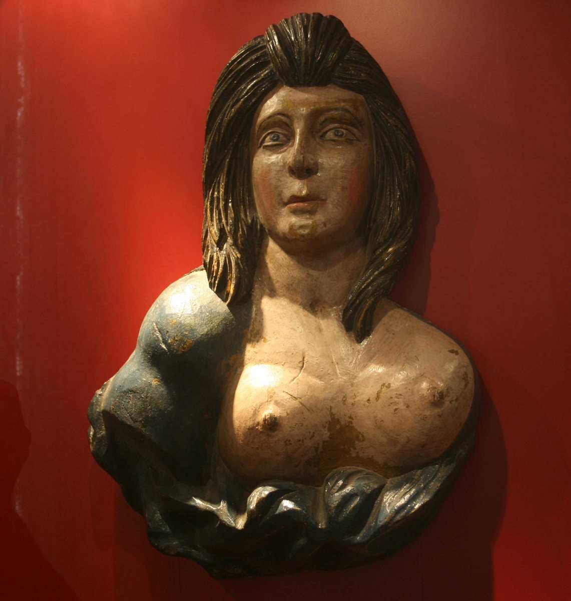 Kvinne med utslått, sort hår  til skuldrene, nakent bryst, draperier under  brystet. Draperi og h. skulder blåmalt. 