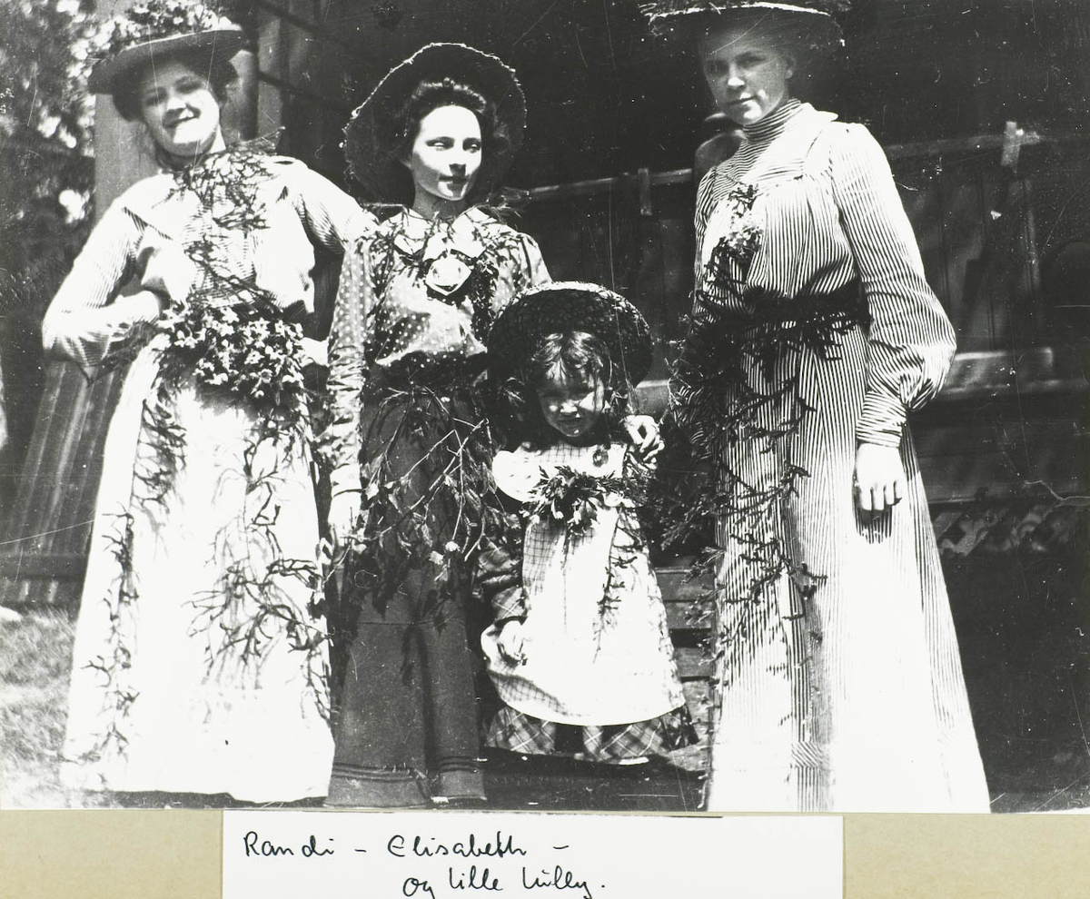 Fire personer, tre damer og et barn. Alle pyntet i flotte kjoler med hatt og blomster