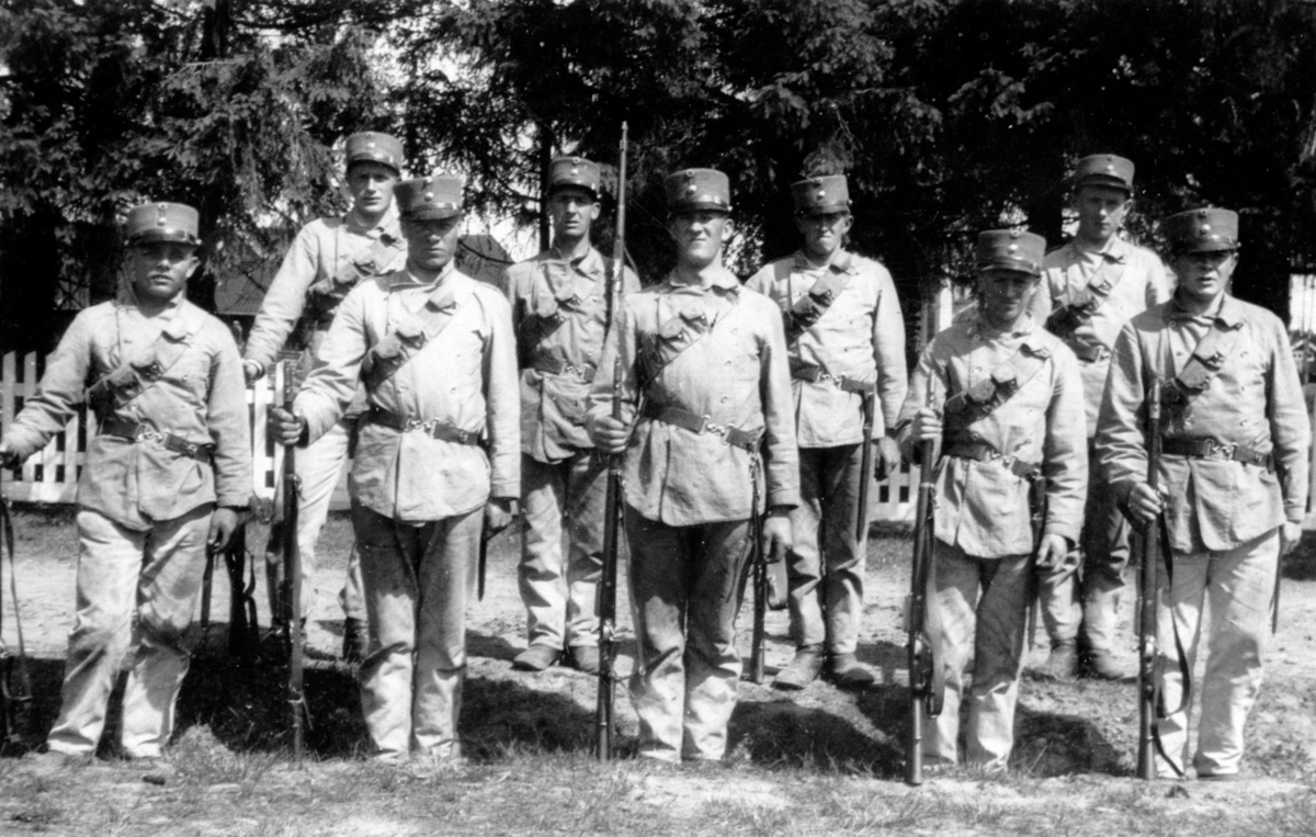 Soldater i arbeidsantrekk, oppstilt med gevær.