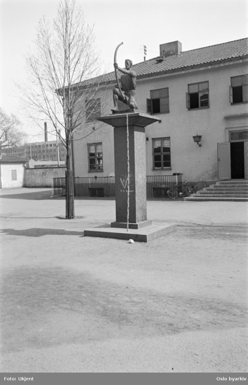 Dyre Vaas bronseskulptur (avduket 1930) "Bueskytteren" på sokkel utenfor klubbhuset ved Dælenenga idrettsplass.