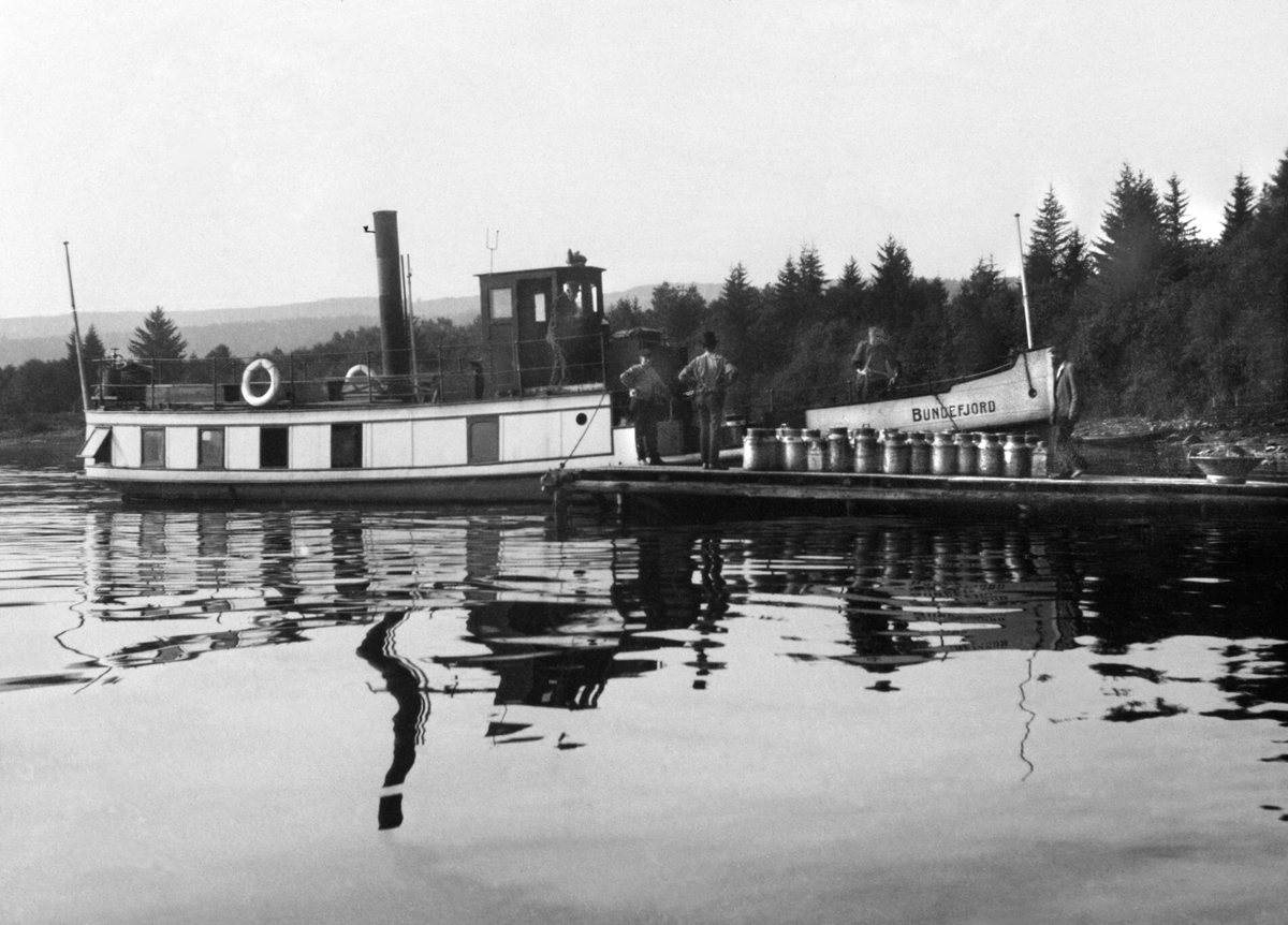 Båten "Bundefjord" i Nerlivika. Laster melkespann ved brygga i Nerlien, Nes, Hedmark. Båten het tidligere "D.S. Prøven".