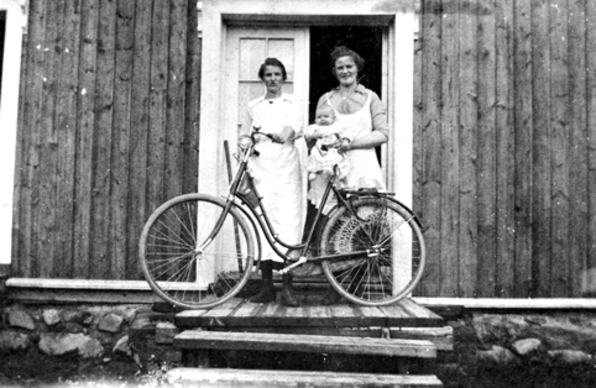 2 jenter med sykkel og lite barn i døra til Rud Samvirkelag, Rudshøgda, Ringsaker.