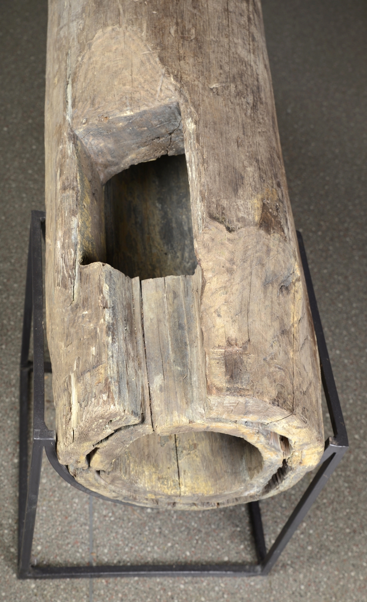 Uthulet tømmerstokk med smidde jernringer. Sylinder for gruvepumpe. To rektangulære stykker er skåret ut i motsatte retninger, ved hver ende av trestokken.