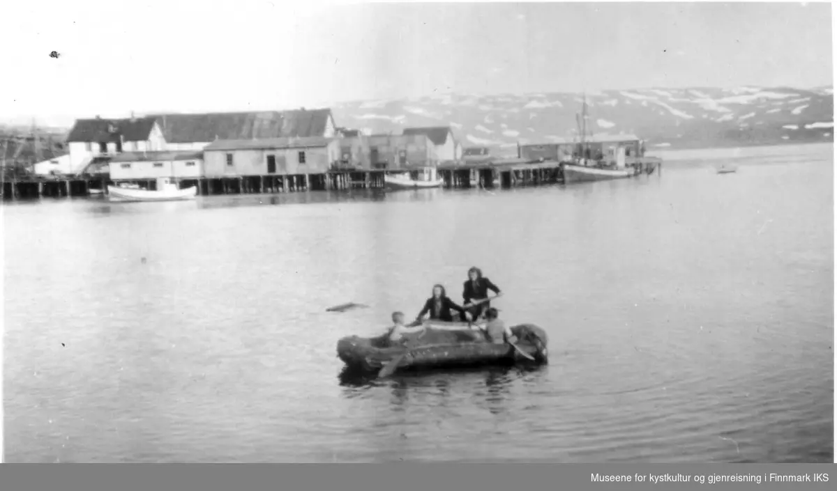 To barn i gummibåt, og to kvinner i robåt på havna i Kongsfjord ca 1946.