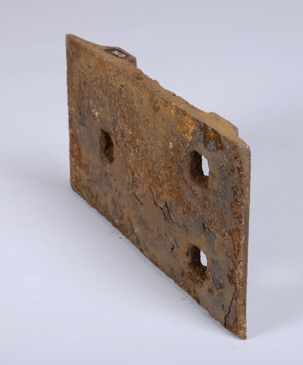 Rektangulær plate i jern med tre hull og spor for ilegg av jernbaneskinne. Platen ble festet med dogg.