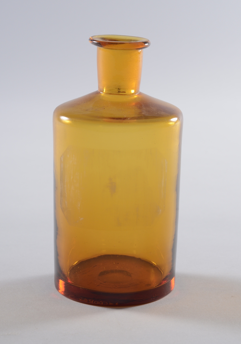 Små sylindriske brune glassflasker med rette skuldre og smal hals, glasspropp med flatt firkantet gripetak.