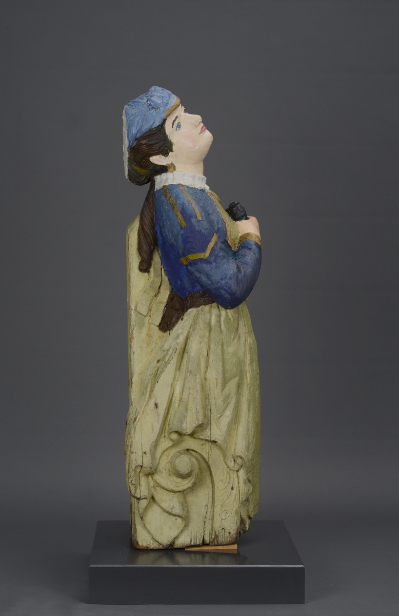 Utskjært kvinnefigur stående på en tresokkel med en kikkert i hånden.