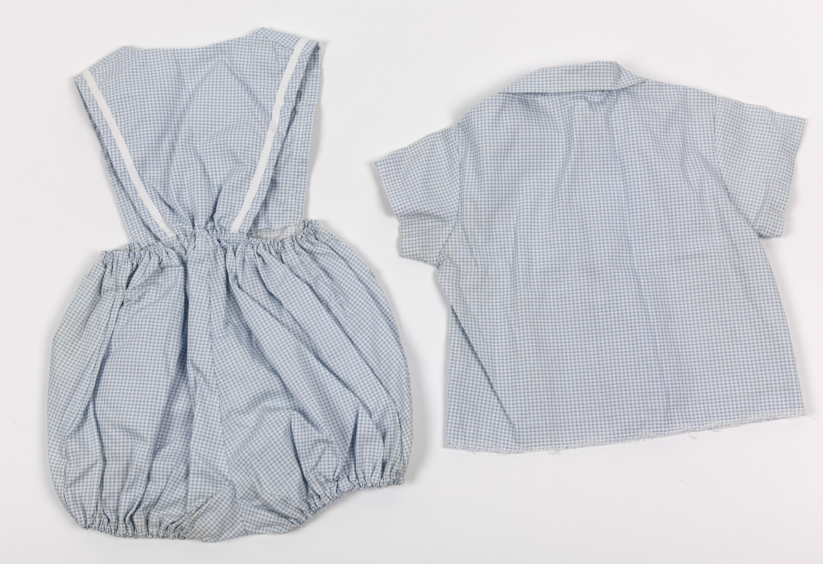 A: Barnebukse. Korte ben, strikk i livet og benåpning, smekke foran og bak. To lommer. Hvite bånd på lommer og smekke. Smårutet mønster.
B: Barneskjorte. Korte ermer. Smårutet mønster.