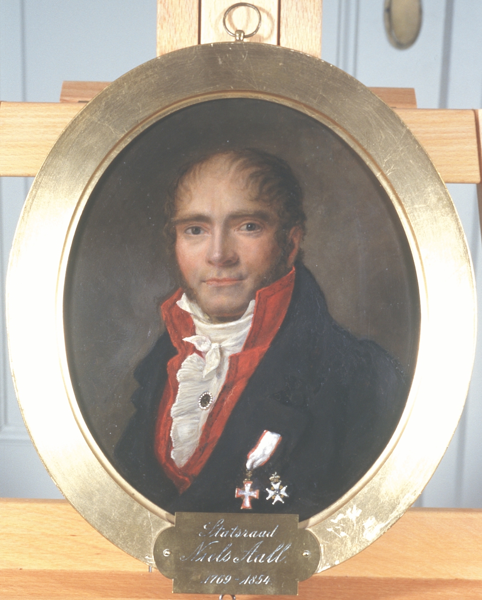 Portrett av statsråd Niels Aall. Mørk drakt med rød vest og hvit skjorte. To ordner festet på brystet.