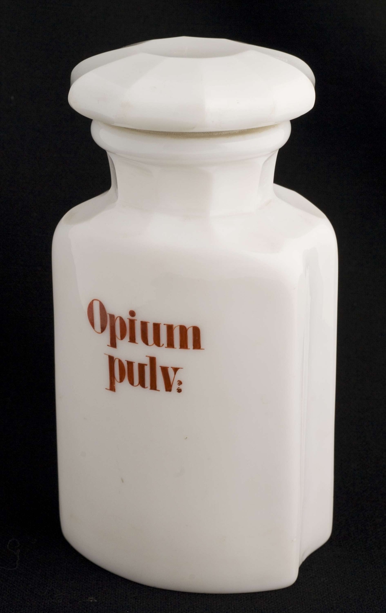 Standglass med propp. 10- kantet propp og hals og skulder . Gripekant på flaske. Halvt gjennomfarget hvitt glass. Rød skrift