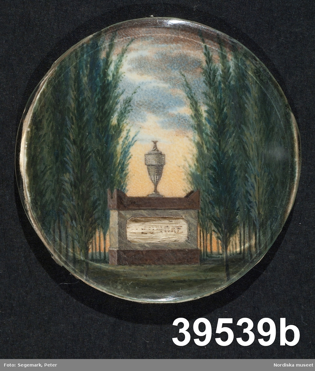 a. Damporträtt, midjebild i profil, vit empireklänning, uppsatt hår.
b. Landskap med gravsten och urna mellan flankerande träd.