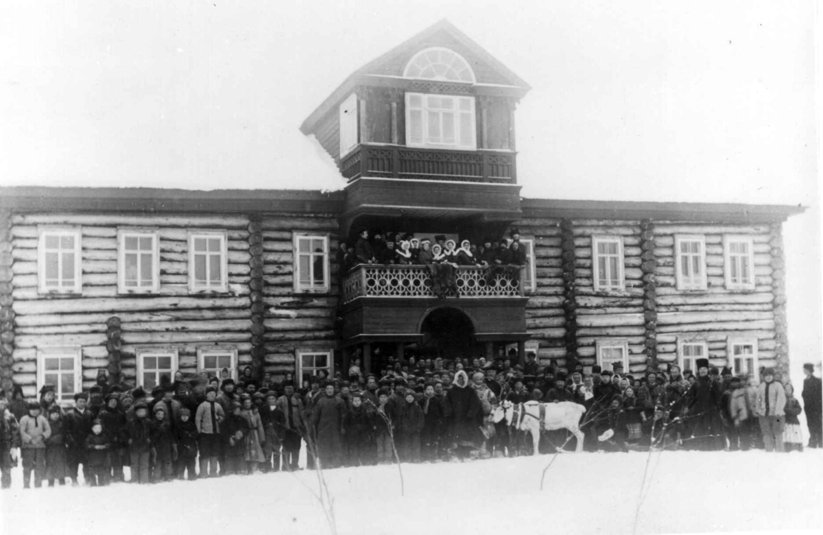 Antakelig klosterskolen i Petsjenga i Russland, nær Kirkenes i Finnmark. Forsamling mennesker med en kjørerein utenfor stor trebygning før 1900.