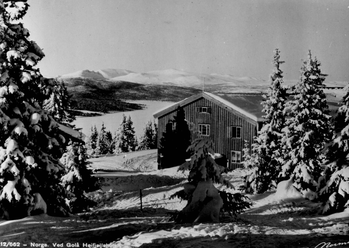 Avfotografert postkort. En stor bygning i nærheten av Gålå høyfjellshotell med flere skispor i forgrunnen. Snødekte grantrær, utsyn over fjellvidder og skogslandskap.
