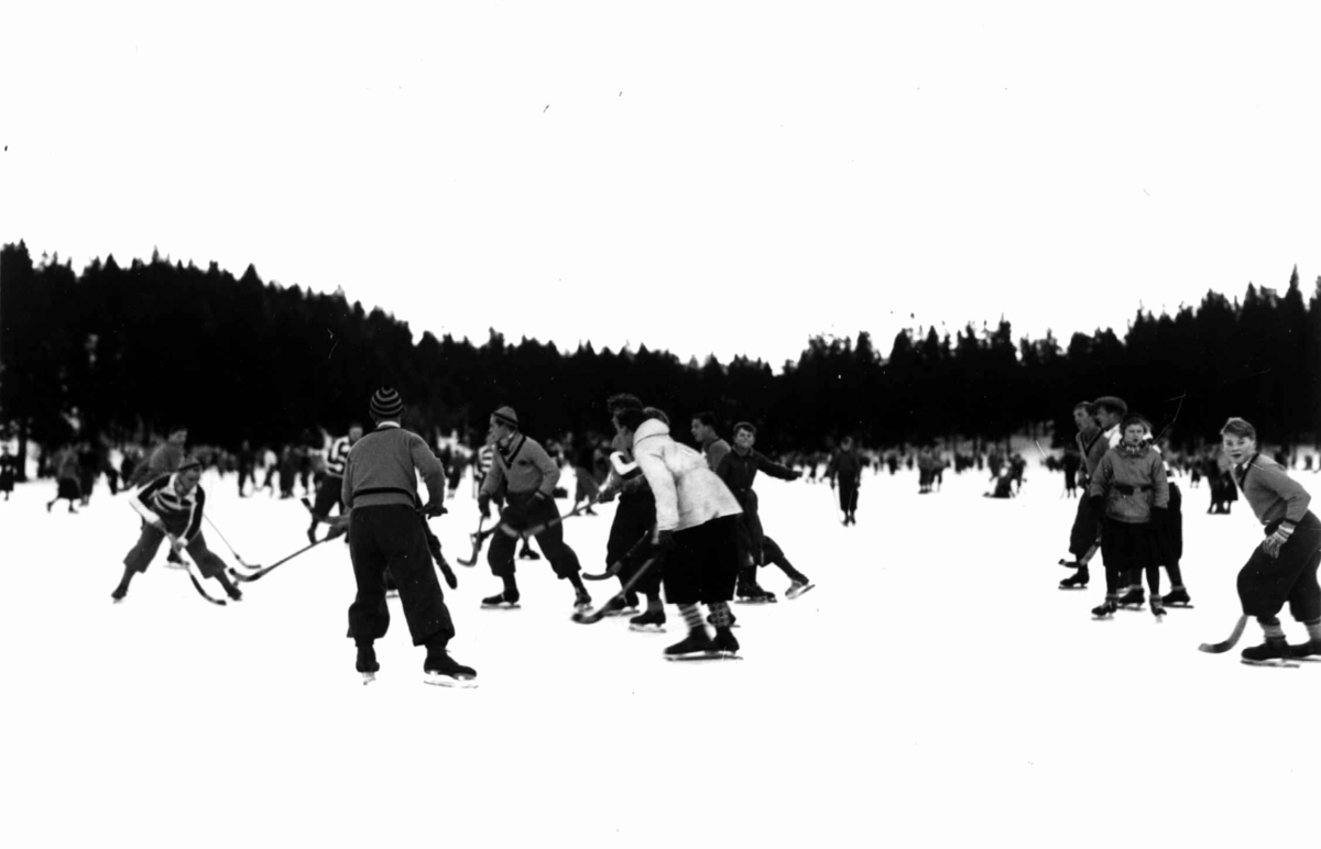 Tryvann skøytebane, Oslo. 1934. Skøyteløpere i sving på isen. Noen med bandykøller.