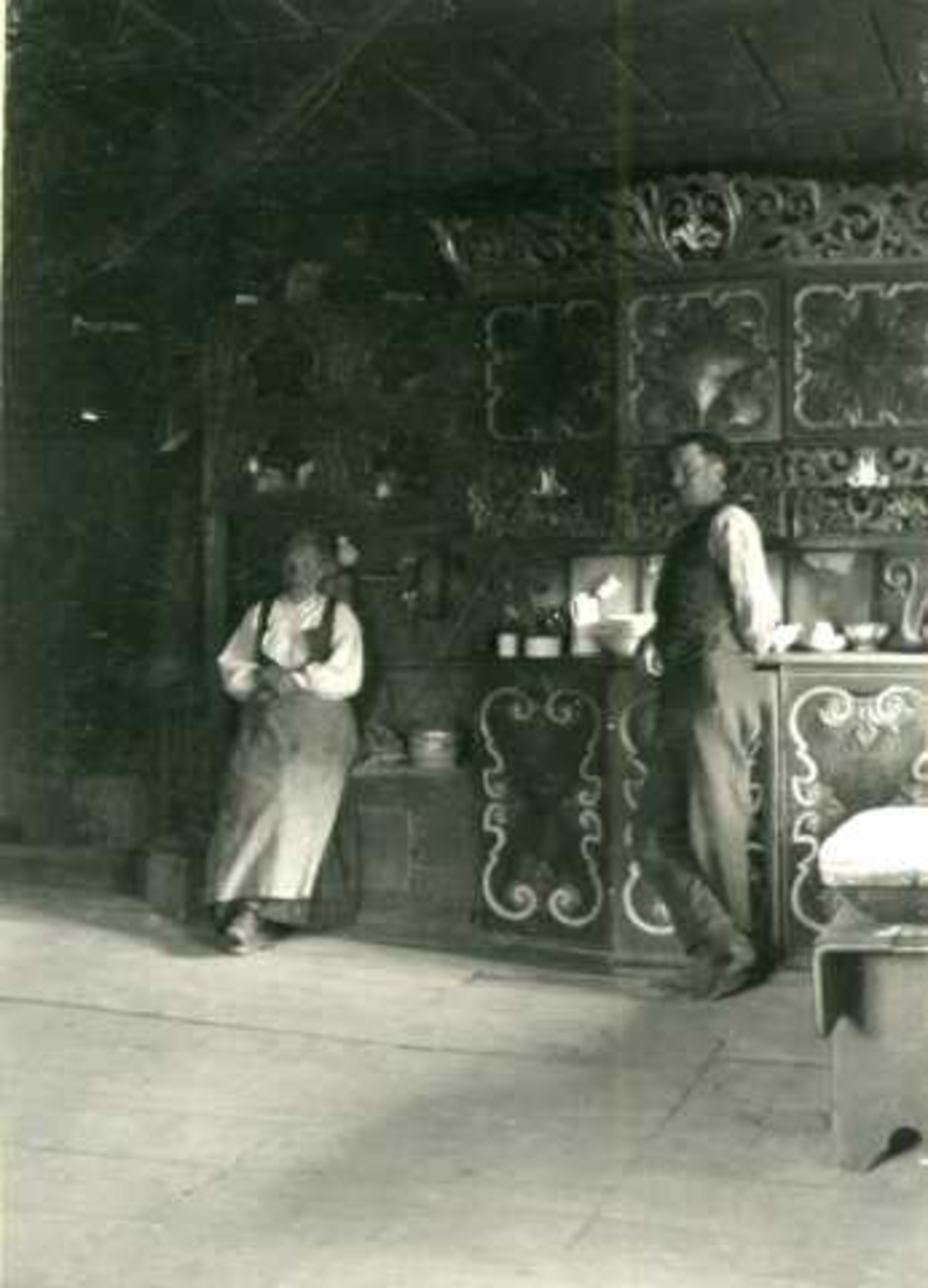Stueinteriør, Nedre Skjåk, Skjåk, Oppland. Kvinne og mann i forgrunnen. Fotografert 1904.