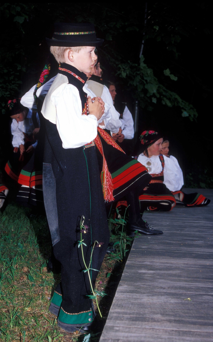 Norsk Folkemuseums dansegruppe, kledd i folkedrakter, danser folkedans i friluftsteateret NF 349. Ung gutt i forgrunnen.
