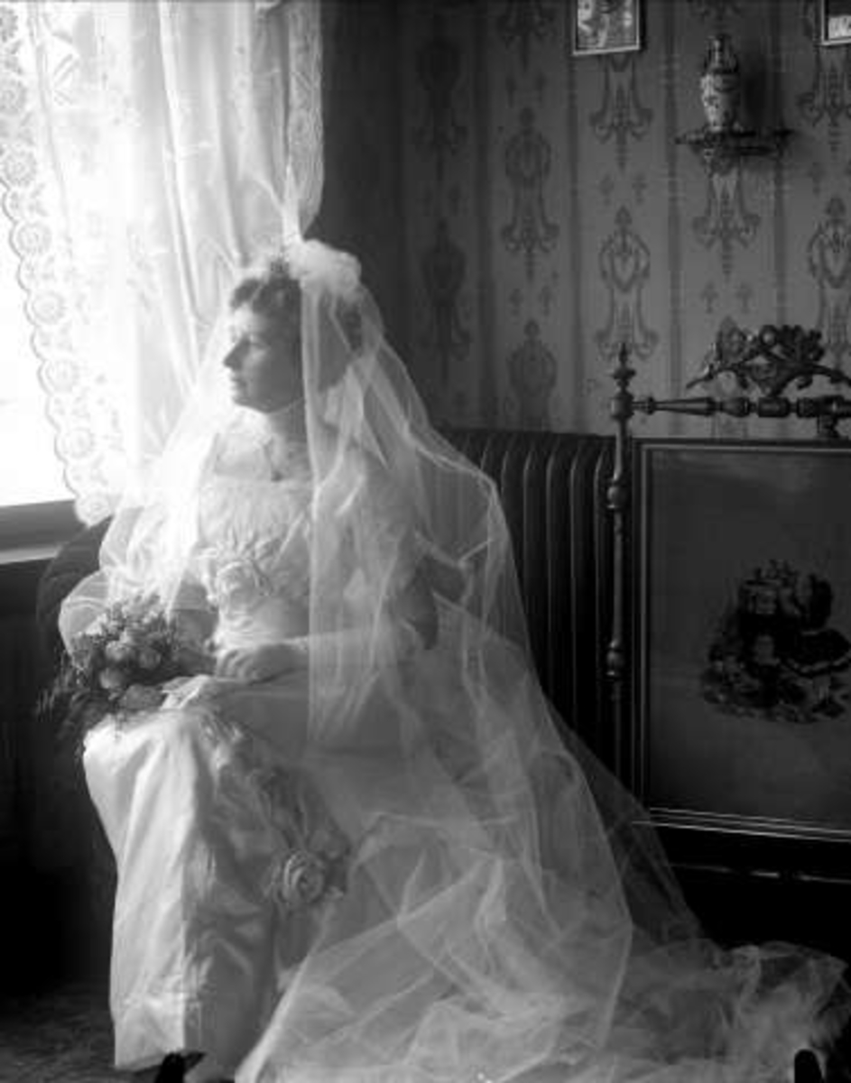 Portrett, kvinne i stueinteriør, i hvit brudekjole med slør. Fru disponent Berrum.
