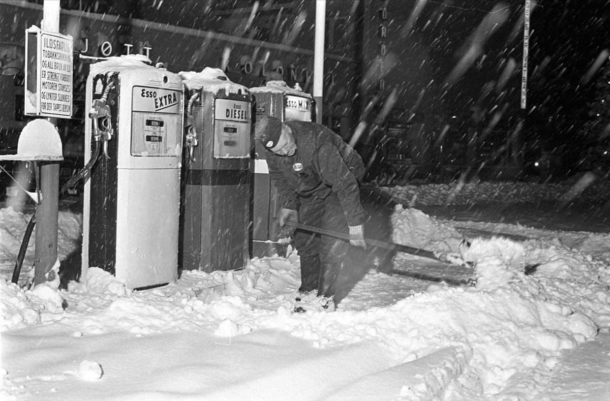 Nysnø, Oslo, 12.12.1962. Mann måker snø på bensinstasjon.