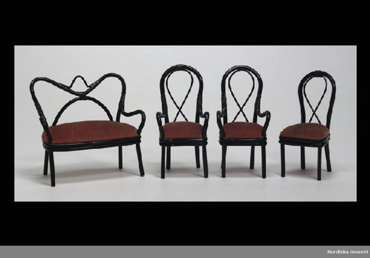 Inventering Sesam 1996-1999:
Möblemang till dockskåp bestående av soffa och 4 st stolar, Thonet-modell, tillverkade av svartmålad rotting, sitsar klädda med röd sammet. 
a) Soffa L 9,5   H 9,5  (cm)
b-c) 2 st  karmstolar H 10 cm
d-e) 2 st stolar H 9,5 cm. 
Tillhör dockskåp från omkr 1840, inv nr 145.505, inrett 1872 av leksakshandlare W A Bandel, Västerlånggatan, Stockholm, för dottern Thyra, vilken vid överlämnandet till museet själv gjort uppställningen av föremålen i dockskåpet.
Birgitta Martinius 1997