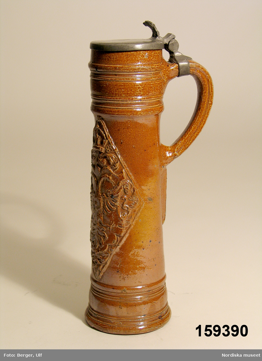 Krus av brunt saltglaserat stengods, så kallad "Schnelle", daterat 1583. Lock av tenn. Tillverkat i Raeren, Tyskland (numera Belgien).
Tegnér 2006