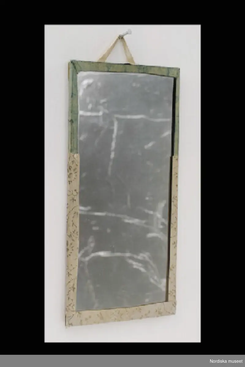 Inventering Sesam 1996-1999:
H 15,5  B 7,5  cm
Fönster av spegelglas, grönt papper uppklistrat på baksidan. Vita upphängningsband. Placerade i dockskåpets översta våning. 
Tillhör dockskåp inv 200.513.
Birgitta Martinius 1996