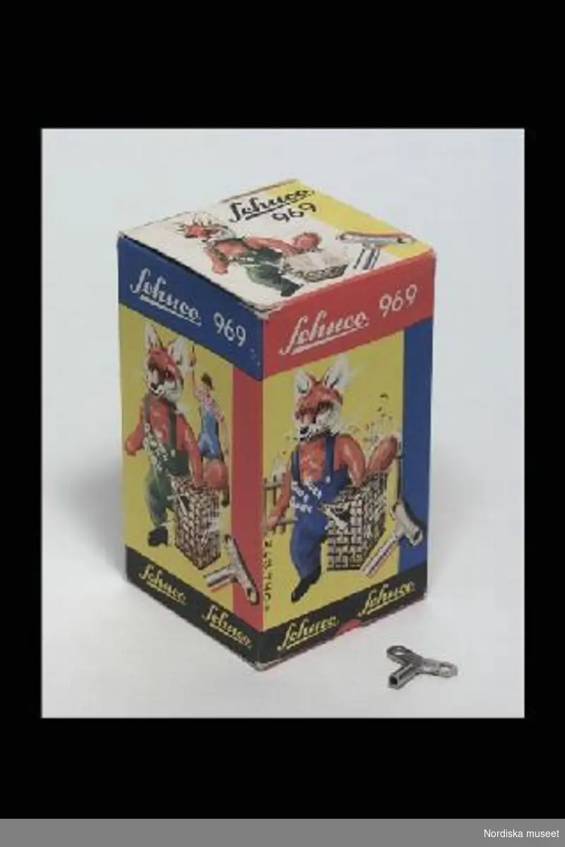 Katalogkort:
"Räv med fjäderverk, leksak. Tyskland omkring 1960. Räv med gås i korg, fjäderdriven leksak, stomme av plåt, plyschklätt huvud, händer och svans, kläder av filt, röd skjorta, gul slips och blå byxor, svartlackerade skor, korg av litograferad plåt, rörligt gåshuvud av plast. Märkt: 'SCHUCO PATENT/MADE IN GERMANY'. lÖS NYCKEL, MÄRKT 'sCHUCO', FJÄDERVERK I KORGEN. Originalask av papp med text och bild i flerfärgstryck, motiv av räv som stjäl en gås och arg bonde som springer efter, text: 'Schuco/969/Made in Western Germany'. Påklistrad prislapp: '10.25. Fabriksny. AW feb 1998." [= anna Womack, inventering Sesam 1996-199]