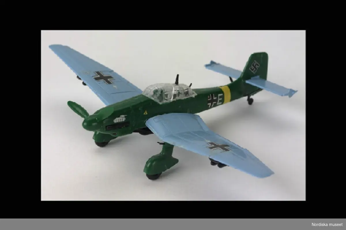 Inventering Sesam 1996-1999:
H ca 4,5 cm
L 14 cm
B 19,7 cm
Modell av tyskt bombplan, Junkers IU 87 Stuka. Grön kropp, Ljusblå vingar. Stjärten dekorerad med hakkors. Lös propeller (ett blad avbrutet). Ställning av ofärgad plast, H 6 cm. med etikett: "JUNKERS JU 87 STUKA". Gjuten märkning: "MATCHBOX".
Placerad på översta hyllan i Mikaels bokhylla, östra väggen.
Ingår i barnrumsinredning inköpt i samband med 1979 års hemundersökning (SAMDOK). Rummet delas av Stefan, f. 1968 och Mikael, f. 1971. Fadern major och modern dagbarnvårdare. Familjen bosatt i radhus i Åkersberga, Vaxholms kommun. Se artiklar i Meddelanden från KU nr 103/1979, SAMDOK-bulletinen nr 8/1979 och Svenska museer nr 1/1980. Intervjumaterial m.m. i arkivet.
Bilaga; förteckning över förvärvet.
AT 1980 [=Annika Tyrfelt]