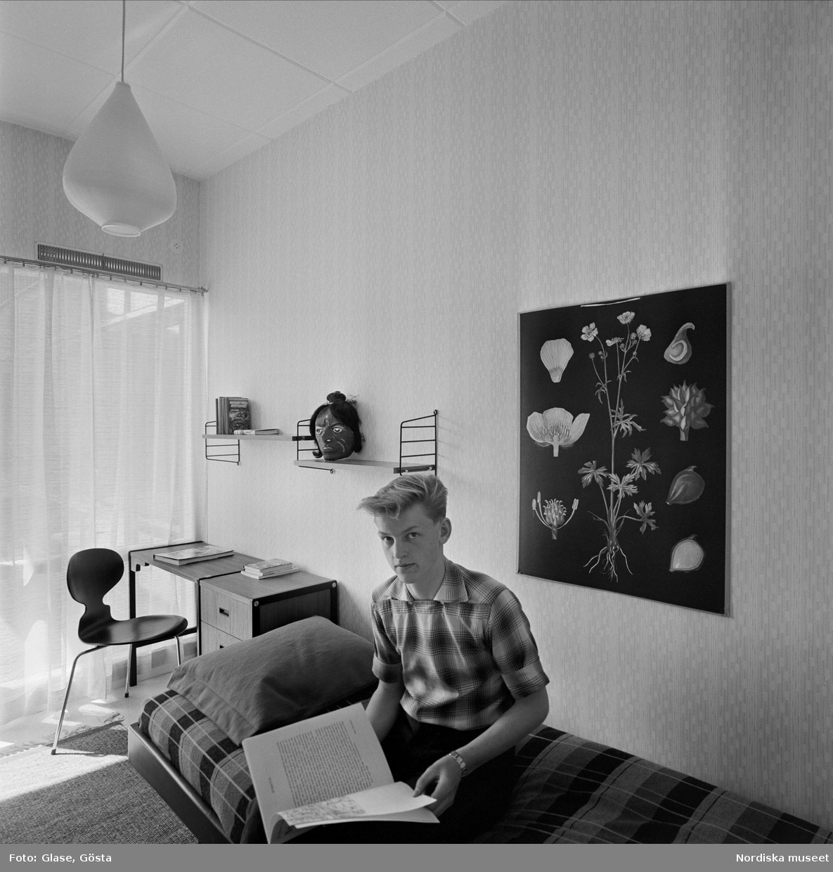 Radhuslänga ritad av arkitekt Bruno Mathsson. Kosta Glasbruk, Småland. Familjen Fagerlunds hus. Pojke sitter på sängen och läser. Myran-stol, String-hylla.