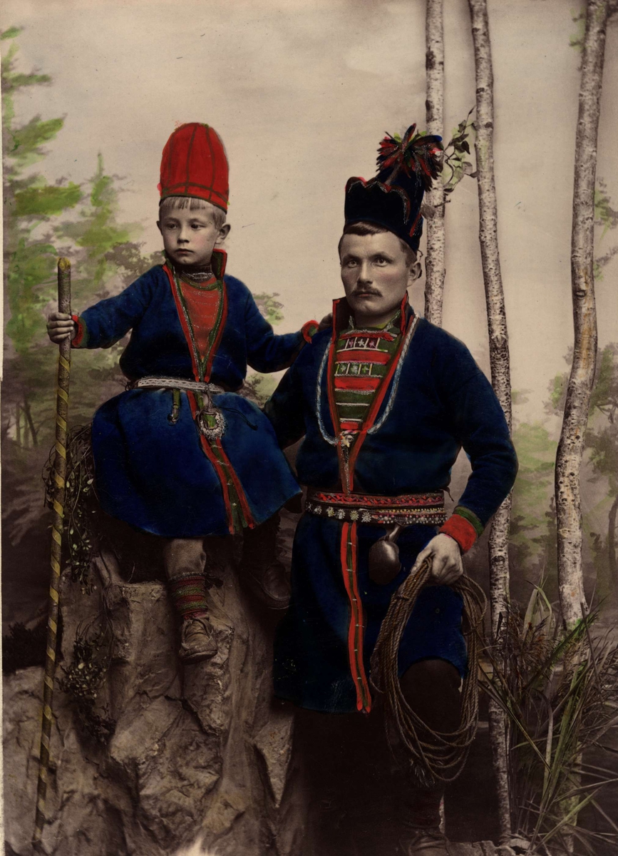 Porträtt av samisk man med son. Nejla och Mattias Åren, Frostviken Lappland. Studiofotografi, handkolorerat.