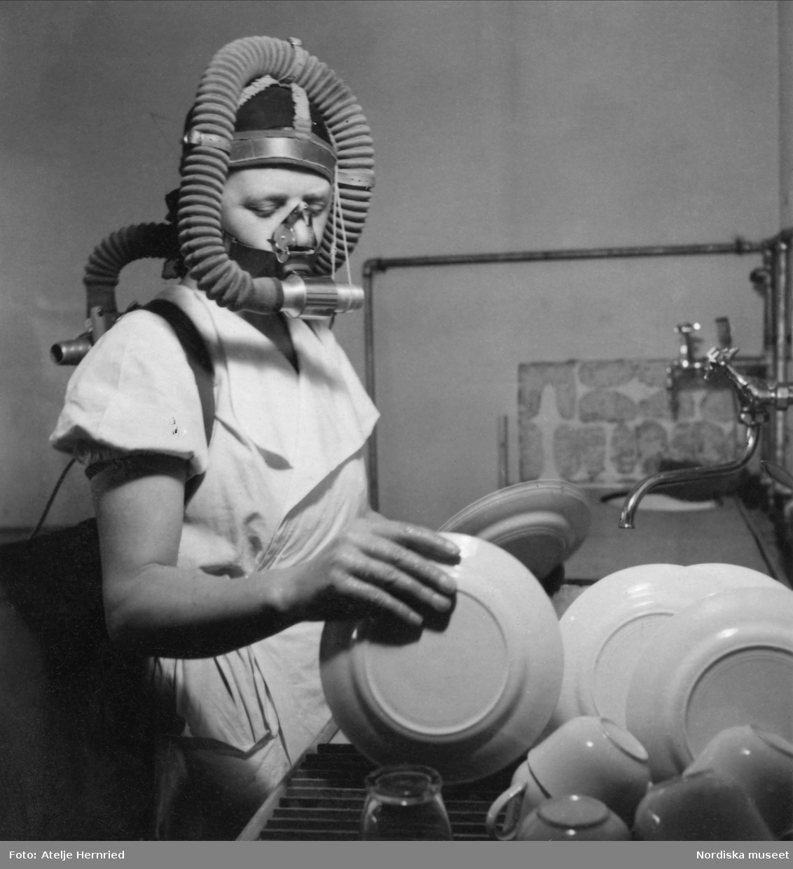 Kvinna i andningsmask diskar i kök. Hemmens forskningsinstitut.