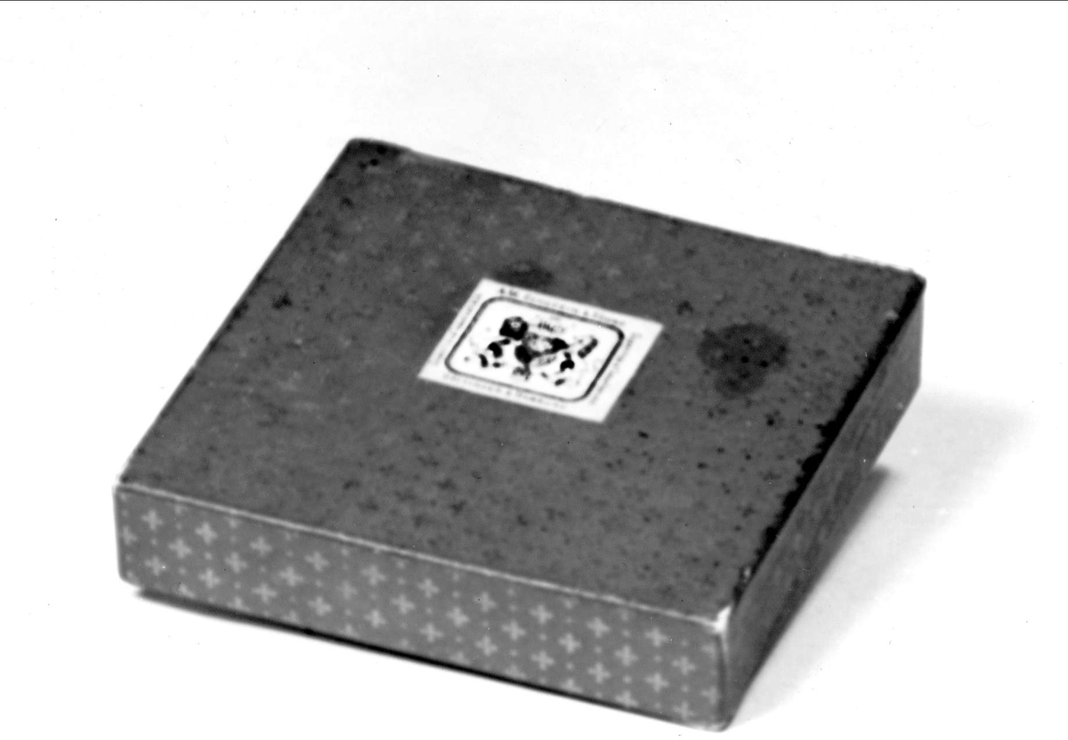 Blå med gulddekor. Vit etikett med text: A.M. Eckstein & Söhns Göttinge & Hamburg. Cigaretten & Tobaksfabriken. På lockets insida etikett i vitt och guld med samma text.