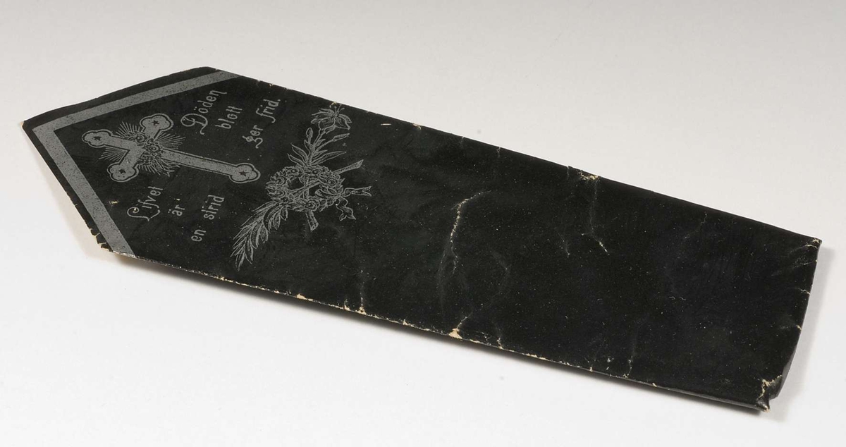 Begravningskaramell av svart glanspapper med tryckt och kors i silverfärg. Text: "Lifvet är en strid".