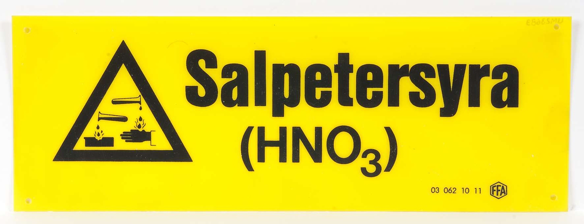 Skylt av gul halvhård plast med svart text: Salpetersyra (HNO3). Varningstriangel med svart ram. Firmamärke: 03 062 10 11 FFA.
