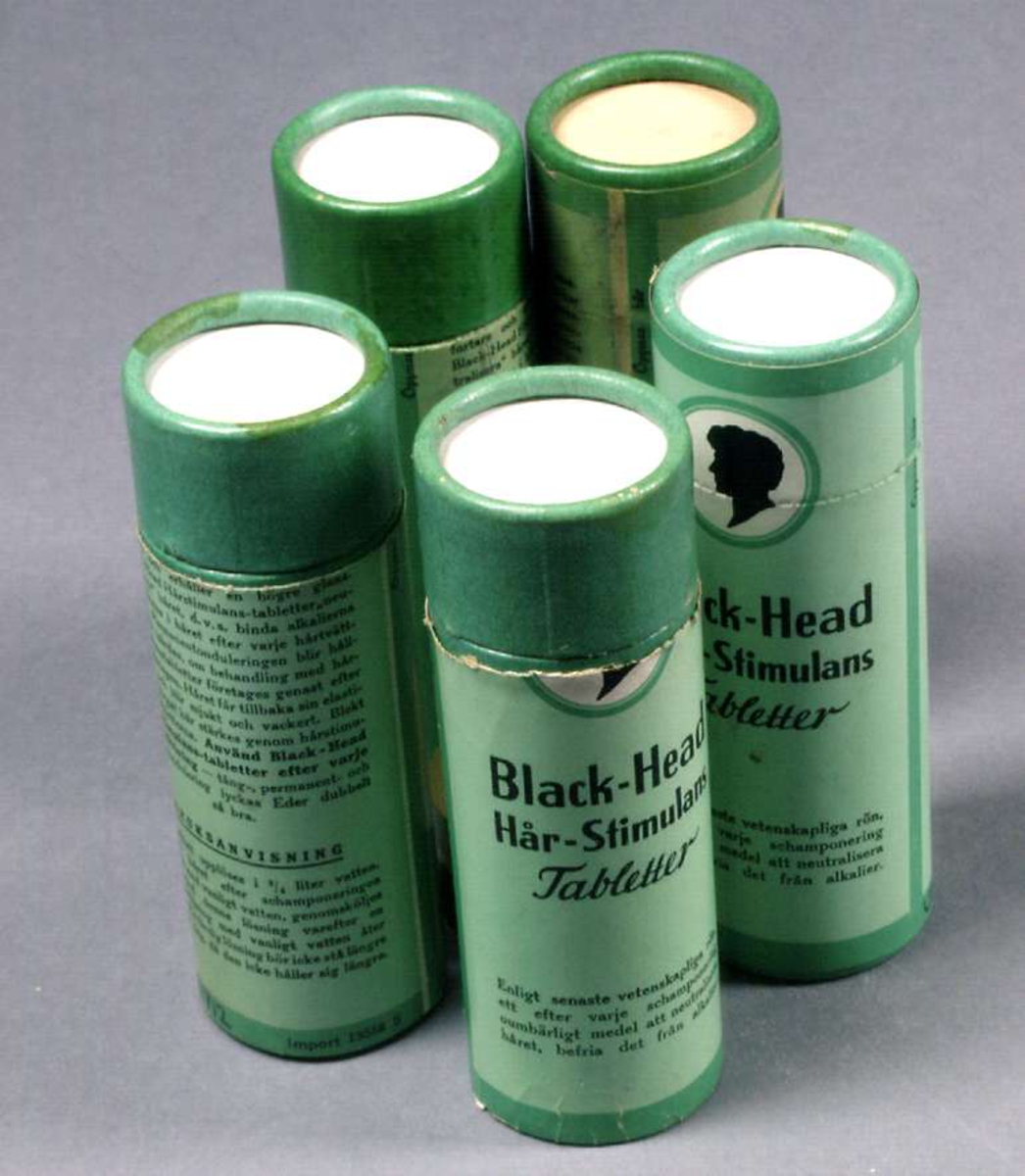 Fyra runda burkar av papp, gröna med svart text: Black-Head Hår-Stimulans Tabletter.
