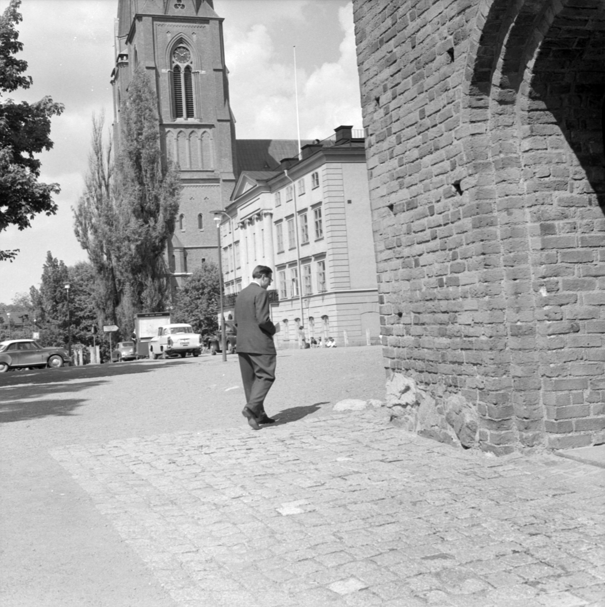Pastor Lars Ridderstedt visar på gamla gravplatser vid Helga Trefaldighetskyrkan som används till bilparkeringar, Uppsala juni 1958