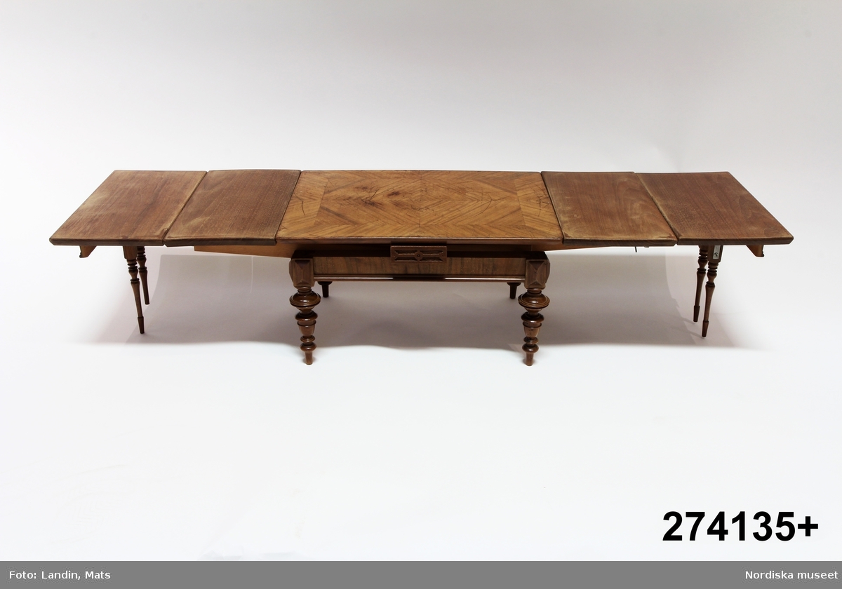 Matsalsbord, modell, omkring 1890, fanerat med valnöt. Svarvade ben. Fyra utdragbara skivor. Två par stödben fälls ut när man drar isär bordets två hälfter.
/Anna Arfvidsson Womack 2022