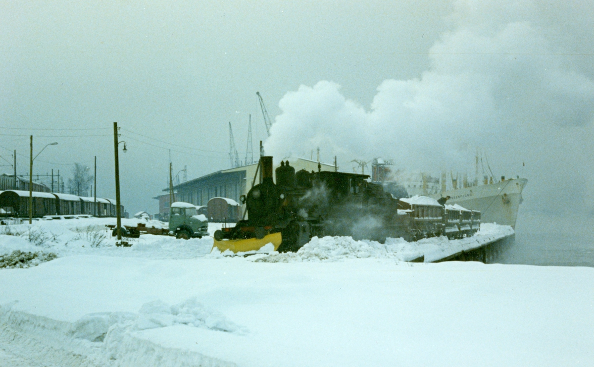 Damplok 21c nr. 377 på Grønlikaia med godsvogner lastet med snø som skal tippes i sjøen. Amerikalinjens M/S Lyngenfjord i bakgrunnen.