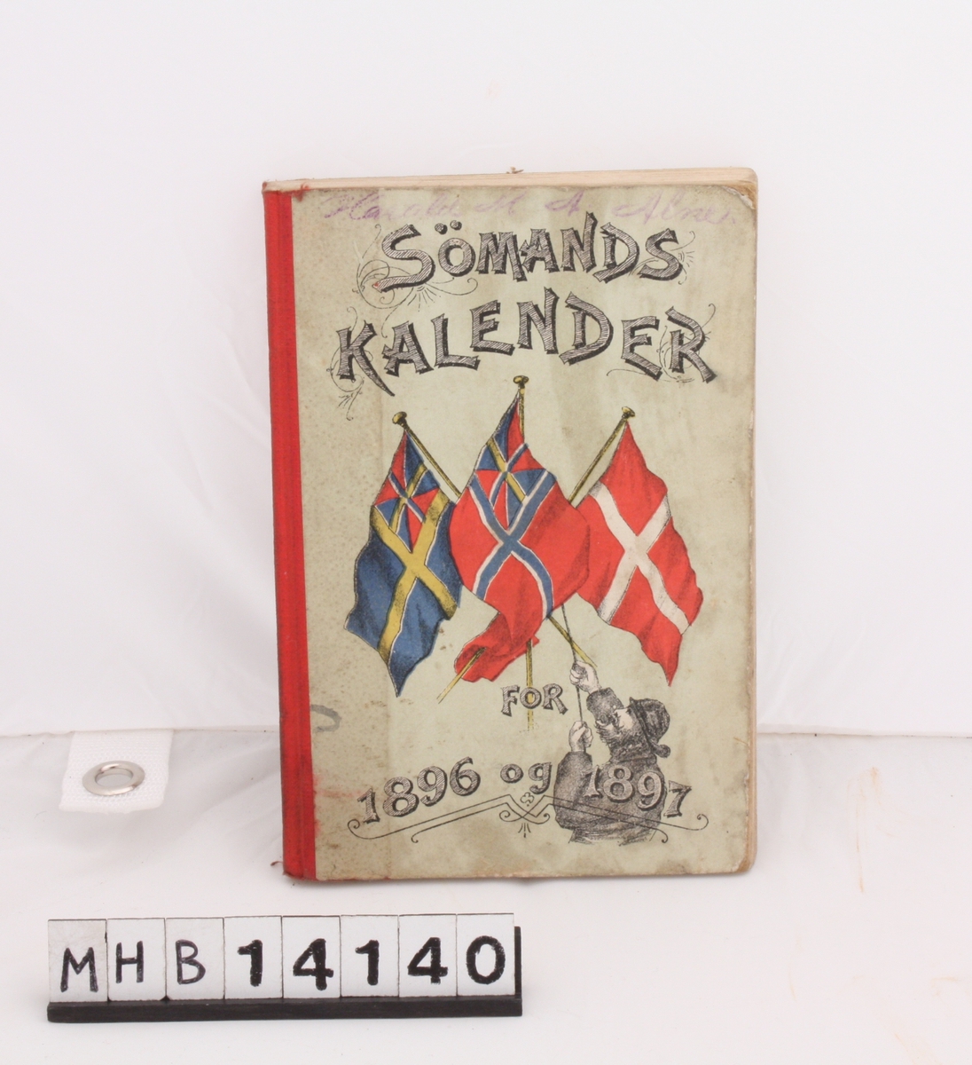 Rektangulær bok med grågrønn innbinding i papp og rød rygg. På forsiden er det danske flagget, samt det svenske og norske, begge med unionsmerket. Boka inneholder kalender og reklame.