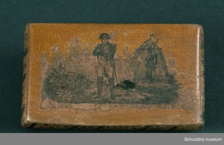 Ur handskrivna katalogen 1957-1958:
Snusdosa
Mått: 8,5 x 5 x 1,8 cm; av trä m. lock på gångjärn; på locket bild av Napoleon I i fält; tuschdekor å öve. sidor. Ngt skad. 

Lappkatalog: 95