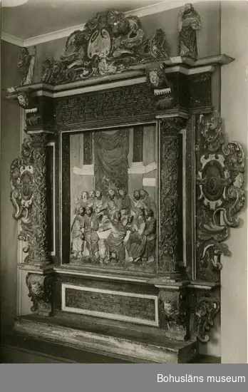 Altaruppsats från 1675, rikt skuren i trä med central skulpturscen, krön, sidostycken, pelare och kapitäl som krederats och målats med mager oljefärg samt förgyllts med oljeförgyllning. Förgyllningen uppvisar både bladguld, slagmetall och förmodligen silver, som mörknat påtagligt. Tillhörande skulpturer överst på ömse sidor om kröndekoren; UM394, UM395.

Centralmotivet skildrar nattvardens instiftande i en skulpturscen. Över scenen läses nattvardens instiftelseord på danska.
Under skultpruscenen inskriften: 
ANNO 1671 ER DENNE KIERKEBYGNING I JESU NAFN BEGYNT OCH UNDER PASTORIS JOANNIS COLSTRIPII FLID MEDH SIT INREDE ANNO 1675 FULBORDET MEDH MIDDEL FRA EGNE RINGE INTRADER, ANDRE GOT FOLCKIS TILHJELP OCH FORNEMMELIG H. KONGL. MAJIT:S WOR ALLERNADIGSTE KONUNG CAROLI XI TILGAWE AFF 150 RIXDALER.

Altartavlan komer från Norra Ryrs kyrka, riven 1873 och benämnd Norra Ryrs kyrka fram till år 1884, idag Lane-Ryrs kyrka. 
UM000384, UM000385, UM000389a-i, UM000393a-i, UM000394, UM000395a-b, UM000401, UM000404a-b, UM000405a-g, UM005660:1-57 samt UM65.01.001 är samtliga inventarier från den gamla kyrkan.

Beskrivning av altaruppsatsens delar:
a. Tavla med nattvardsframställning; h. 120, br. 104 cm
b. Överdel; l. 224 cm
c. Krön till överdel; br. 132, h. 58 cm
d. Pelare; h. med platta över kapitälet 113 cm
e. Pelare, som föregående h. 113 cm
f. Sidostycke; i 2 delar I-II, h. med tappar 128, br. 67 cm
g. Sidostycke; i 2 delar I-II, h. med tappar 131, br. 69,5 cm
h. Underdel; l. 201 cm
i. En lös del, tillhörande UM000393h

Altaruppsatsen ska enligt uppgift i artikel i Bohusläningen den 30 april 1963 vara skänkt till församlingen av Karl XI som ett led i försvenskningen av Bohuslän.

Ytterligare foto i Uddevalla museums kyrkliga utställning år 1920, se UMFA53292:0013, UMFA53710:0075.

Ur Nationalencyklopedin, NE.se: Altarprydnad
Under 1500-talet utbildades i Italien en ny typ: en central målning eller skulptur, omgiven av en rik, klassiserande omramning. I den tyska renässansen utvecklades altarprydnaderna till altaruppsatser, som med kvardröjande gotisk höjdsträvan byggdes upp i flera våningar. Centrala bilder, målade eller skulpterade, av (nedifrån räknat) nattvarden, korsfästelsen, uppståndelsen och himmelsfärden omges av en arkitektonisk ram med slösande rik ornamentik, allegoriska figurer av dygderna, änglar med pinoredskap etc. Denna typ blev vanlig i Norden under 1600-talet och utformades t.ex. av Jacob Kremberg, Lund, och Marcus Jäger, Göteborg.

Ur handskrivna katalogen 1957-1958:
Altartavla, Lane Ryr
a) Tavlan m. nattvardsframställn. H. 120; Br. 104 cm. b) Överdel, L. 224 cm. c) Krön t. överdel, Br, 132; H. 58 cm. d) Pelare, H. (m. plattan över kapitälet) 113 cm. e) Pelare, som  föreg. H. 113 cm. f) Sidostycke, H. (m. tappar) 128 cm; Br. 67 cm; i 2 delar I-II. 
g)  Sidostycke, H. (m. tappar) 131; Br. 69,5 cm; i 2 delar I-II. h) Underdel, L. 201 cm. i) En lös del, tillhörande U.m 393 h.

Lappkatalog: 13

Litt.: Gardell, Sölve: Den kyrkliga konsten i Uddevalla museum. Vikarvet 1933. 
Altaruppsats från 1600-talet åter i bruk i Lane-Ryrs kyrka. Artikel i Bohusläningen den 30 april 1963.
Kristiansson, S.: Uddevalla stads historia, del I, s. 338-339.
Oedman, Johan Chorographia Bahuensis. Thet är Bohus-Läns Beskrifning. 1746. Faksimil- tryck 1911, s. 110.