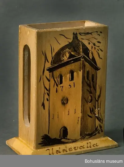 För stor tändsticksask. I sidan öppning för plånet. Framsidan pryds med bild av Uddevallas kyrkas klocktorn, samt på sockeln namnet "Uddevalla".

Se UM015810