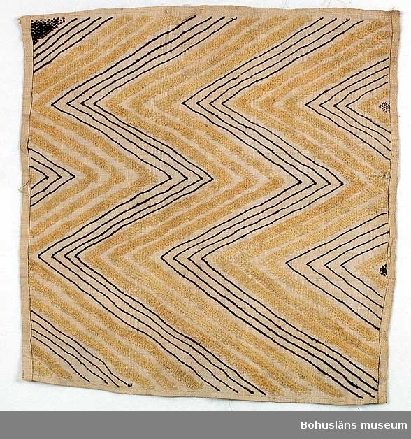 Text till webbutställning "Från när och fjärran" presenterad på Bohusläns museums hemsida år 2009 - 2013:
Vävnad av rafiabast med broderat mönster, delar av mönstren har flossakaraktär, 67 x 60 cm.
Mönstren, som täcker hela den vävda tuskaftsbottnen, består dels av linjer, dels av ytor med sammets- eller flossakaraktär. Typisk är att mönsterformerna plötsligt ändrar karaktär och symmetrin saboteras på ett befriande sätt. Baksidan är nästan enfärgad, broderiet syns endast i svag relief. 
Basten kommer från rafiapalmens långa blad, Rafhia farinifera. Bladen kan bli upp till 20 meter långa. I Sverige träffar vi på materialet under benämningen trädgårdsmästarbast. 
Textilier av detta slag utfördes i Kasai-området i södra delen av Belgiska Kongo, nuvarande Demokratiska republiken Kongo. Där fanns från 1600-talet Kuba-riket med Shoowa-stammen, som var känd för sin mycket speciella och högt skattade broderiteknik. Det var männen som vävde, medan kvinnorna broderade de geometriska mönstren i dessa prestigetextilier, ibland använda som betalningsmedel.
Gåva av Sjökaptenen och Riddaren Elmer Göransson år 1961.

Uppgifter om givaren
Under sin 30-åriga vistelse i Belgiska Kongo skötte Elmer Göransson (1872-1964) under många år transporter på landets floder. När han år 1932 avslutade sin tjänstgöring var han både skeppsfartygsinspektör för hela den belgiska flottan i övre Kongo, t. f. chef för hydrografiska tjänsten samt hamnkapten i Leopoldville.
Han var samlare av bl.a. vapen, textilier och träkärl. I omgångar från 1919 skänkte Göransson afrikanska föremål till Uddevalla museum. Han kom att bli en av museiföreningens hedersledamöter.
Vid sin bortgång 1964 var han bosatt i Kungsbacka.

Artikel i Bohusläningen från måndagen den 1 november 1937.
"Vittberesta bohusläningar berätta. Upplevelser under 30-årig vistelse i Belgiska Kongo. Kapten Elmer Göransson. Folk och sedvänjor under ekvatorns glödande sol."
_______________________________________________________________________

Kontinent: Afrika
Information på lappkatalogkort:
Matta, 67 x 60 cm. Geometriskt mönster i gult och brunt på blekskär botten. Av rafia. Flossaliknande. Teknik som 61.03.076. Congo, Afrika

Enligt litteraturen är vävnader av detta slaget utförda av stammar som levde i området Kasai i södra delen av forna Belgiska Kongo, senare Zaire. Man pratar om det på 1600-talet bildade Kuba-riket. Ett folk inom Kuba, Shoowa-stammen, var kända för sin mycket speciella och högt skattade broderiteknik.
Det var männen i Shoowa-stammen som vävde, medan kvinnorna broderade de geometriska mönstren.

Sicksackformat broderat mönster i gult och brunt mot ljusare gulvit tuskaftsbotten. Flossakaraktär på delar av broderiet.
Stadkanterna på vävnaden är vikta och fållade mot framsidan med förstygn; i längdriktningen är fållen vänd mot baksidan och sydd med förstygn.

Litteratur: Artikel i Hemslöjden nr 4/1990, "Den saboterade symmetrin", Olle Nessle, s. 14-15.

Uppgifter om E. Göransson i Knut Adrian Anderssons katalog samt historik om samlingen: Se UM61.03.001

In English: Cut-pile raphia cloth, the so-called Kasai velvets. Bakuba, Zaire.