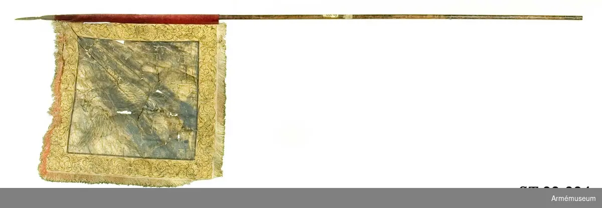 Duk av linneväv helt bemålad på båda sidor med guldfärg och dekor tecknad med svarta konturer. Mittenmotivet är en örn med silhuetten av en stad under sig. Bård med slingrande växtmotiv. Röd silkesfrans runt tre sidor av duken.