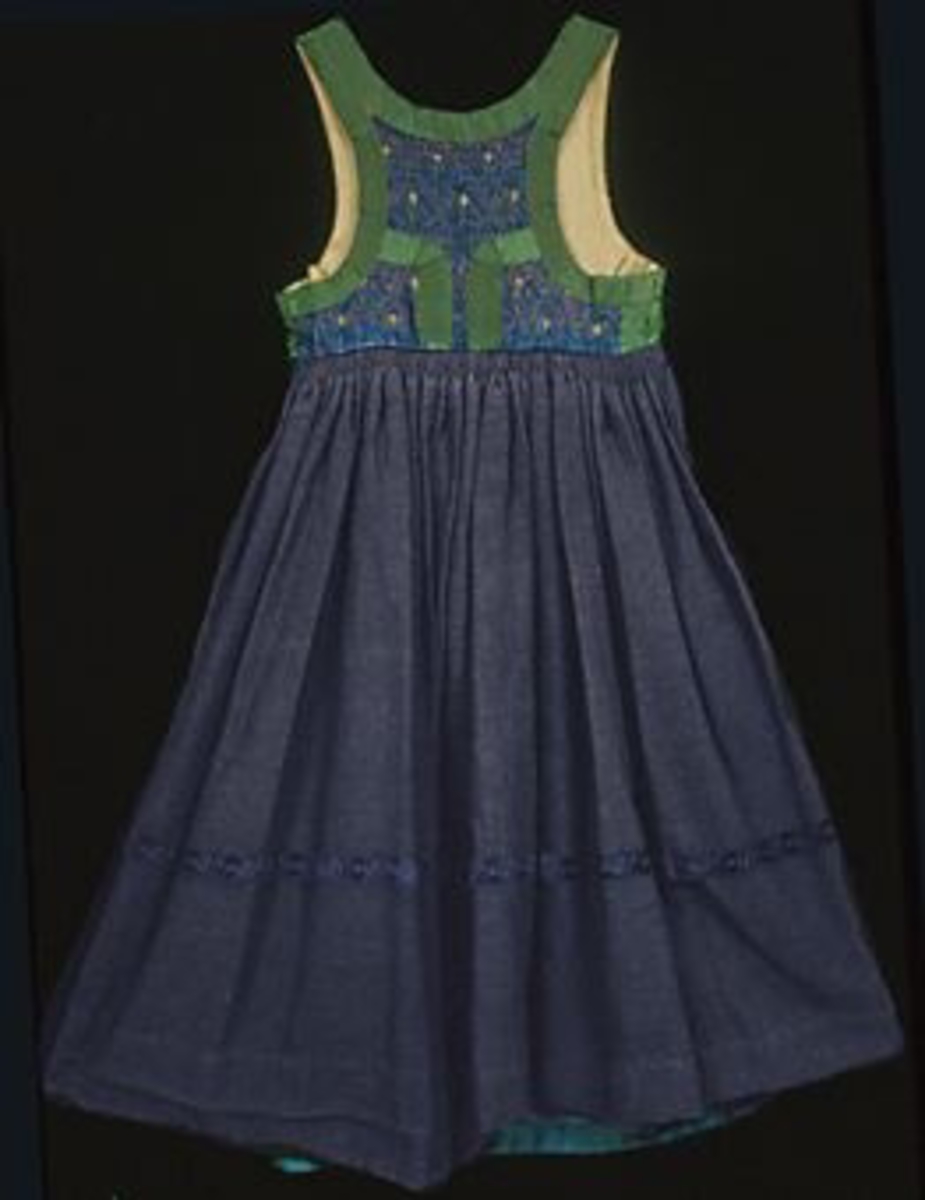 Livkjol med mönstrat, bandkantat liv och mörkblå kjol. Livstycket är sytt i mönstervävt tyg med blå bomullsvarp och rosa silkeinslag. Ytan är dekorerad med plattsömsbroderi i form av gula stiliserade blommor och gröna prickar, stygnen har sytts genom två tyglager; ett mellanliggande tyg i oblekt linne. Livet är kantat och dekorerat med ett grönt ca 35 mm brett ripsband. Bakstycket har två påsydda gröna band som bildar en svängd V-form, vecken har sytts ned med flätsöm i grönt. Livet är sytt av ett bakstycke och två framstycken, det är helfodrat med oblekt linneväv i tuskaft. Mitt fram, intill öppningen på vardera framstycke är tre silvermaljor fastsydda, en av dem är något större än de övriga. Öppningen fortsätter i ett 270 mm långt sprund på kjolen. Sprundet knäpps med en tryckknapp och en hyska och hake, ovanför haken sitter ytterligare en hake med en trådögla. Kjolen är sydd i blålila tuskaftad oberedd ylleväv av tre våder; en fram och två bak. Ett blått 30 mm brett mönstrat sammetsband är påsytt runt om på kjolen 300 mm ovanför fållen. Kjolvidden är samlad i små rynkor längs hela bakstycket. I sidorna har livet tagits in, tyget har vikts i ett veck som hålls ihop med en enkel söm, kjolens rynkor ligger i dubbla lager. Kjolfållen är skodd invändigt med en 110 mm bred remsa i blått bomullstyg, sprundet mitt fram är också fodrat med blått bomullstyg. Sidficka samt kantning av kjolens sömsmån upptill i rutigt blått bomullstyg. Kjolen har varit avkortad/uppvikt och fållad ytterligare en gång, fållen har nästan helt släppt. Liv längd: 390 mm. Kjol längd: 890 mm. Kjol vidd: 2680 mm. Kjolen är ihopsydd på maskin, övriga sömmar är handsydda.