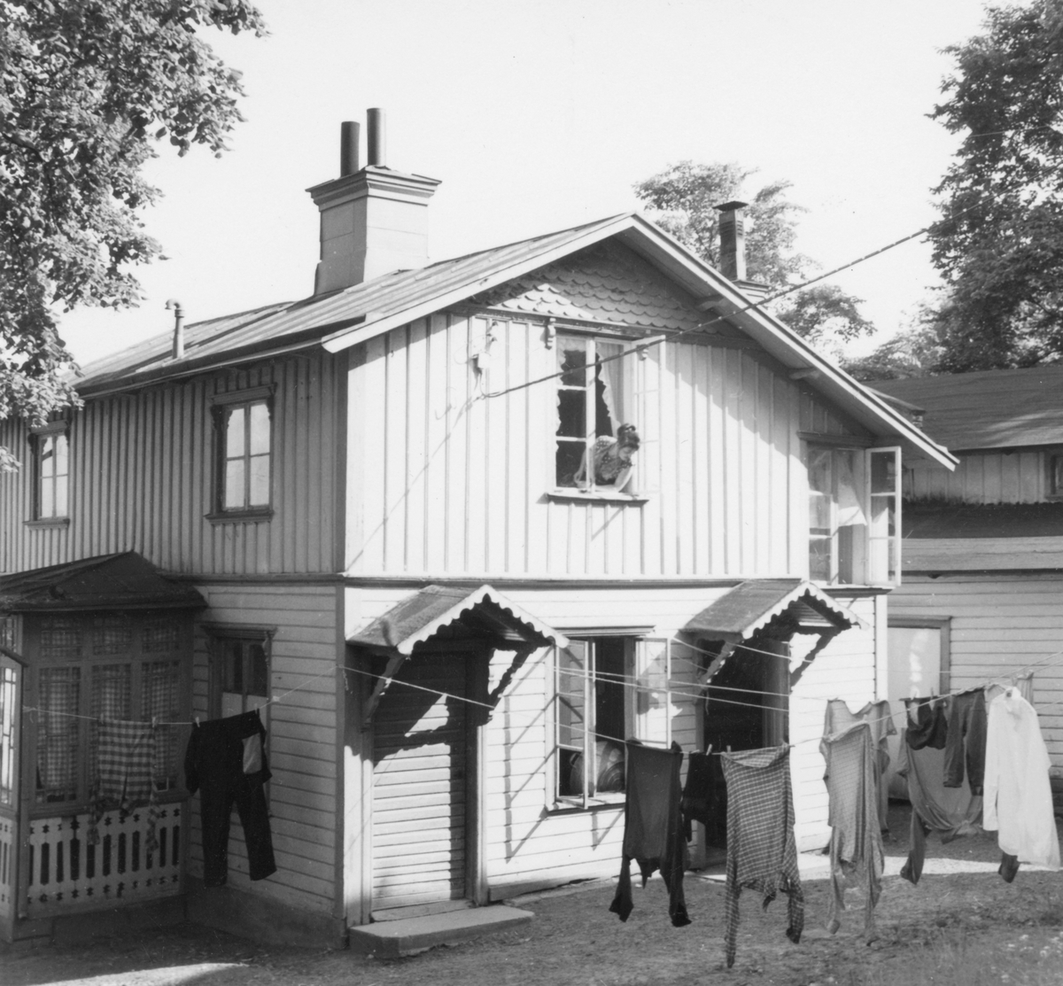 Ett hus med gård i Jönköping. Tvätt hänger på tork och en kvinna tittar ut genom ett fönster på övervåningen.