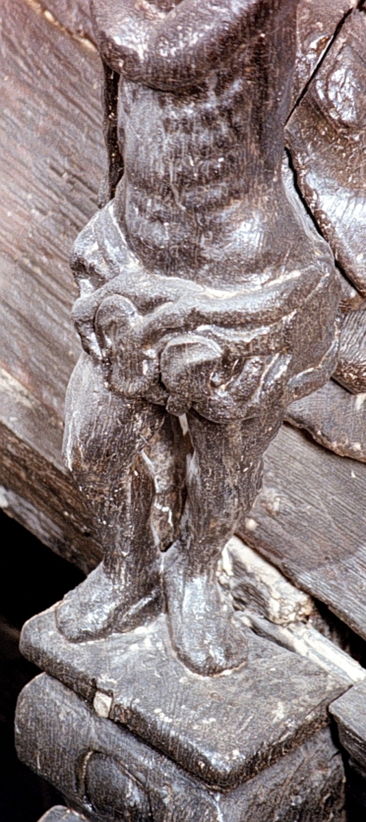 Skulptur av en naken man, så kallad vildman, stående på hög sockel.

Bålen är frontalställd medan huvudet är kraftigt lutat åt vänster och något vridet. Vildmannen har långt skägg och en virad turban på hjässan. Kring livet bär han en gördel sammansatt av växtdelar. Utmed höger sida håller vildmannen med bägge händer en lång klubba med förtjockad nederända. Kroppstyngden vilar helt på vänster ben och höft, sistnämnda markant utskjuten. Högerbenet är böjt och fötterna placerade tätt intill varandra. Figuren står inte mitt på ståplattan utan är förskjuten något åt sidan.



Sockeln är horisontell upptill och snedskuren nedtill, med en grotesk maskaron under en rektangulär vulst med utbuktande ändar. Figuren är rundskulpterad medan sockelns baksida är plan. Basen är horisontal.



Skulpturen är mycket välbevarad.



Text in English: Sculpture of a half-naked man standing on a high pedestal.

The torso is shown en face whilst the head is sharply bowed and turned to the left. The figure has a long beard, wears a turban on his head and a girdle of vegetation around the waist. With both hands he holds a long club, which widens at the base, at his right side. The weight of his body rests wholly on his left leg, his left hip is pronounced. The right leg is bent, the feet are close together. The figure does not stand in the centre of the pedestal but is placed a little to the side.



The pedestal has a rectangular horizontal entablement and a grotesque mask beneath the beading. While the figure is sculpted in the round, the back of the pedestal is flat.



The sculpture is very well preserved.