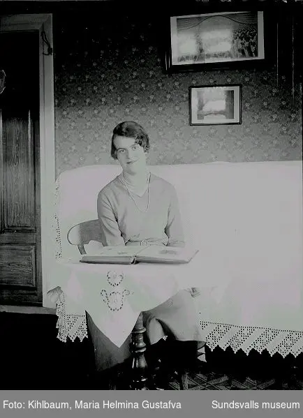 Porträtt. Kvinna i rumsmiljö, sitter vid ett bord med ett fotoalbum uppslaget.