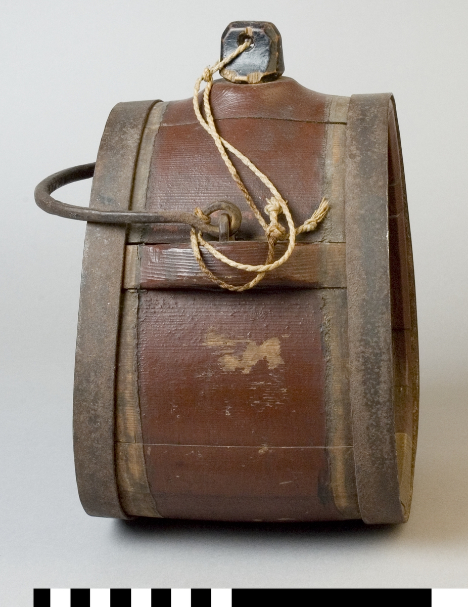 Mjölkflaska av trä, målad brun. Med band och handtag av järn. Med tillhörande propp av svartmålat trä. 
Märkt på ena sidan 1883, i vitt.
Märkt på andra sidan "JMS", i vitt.